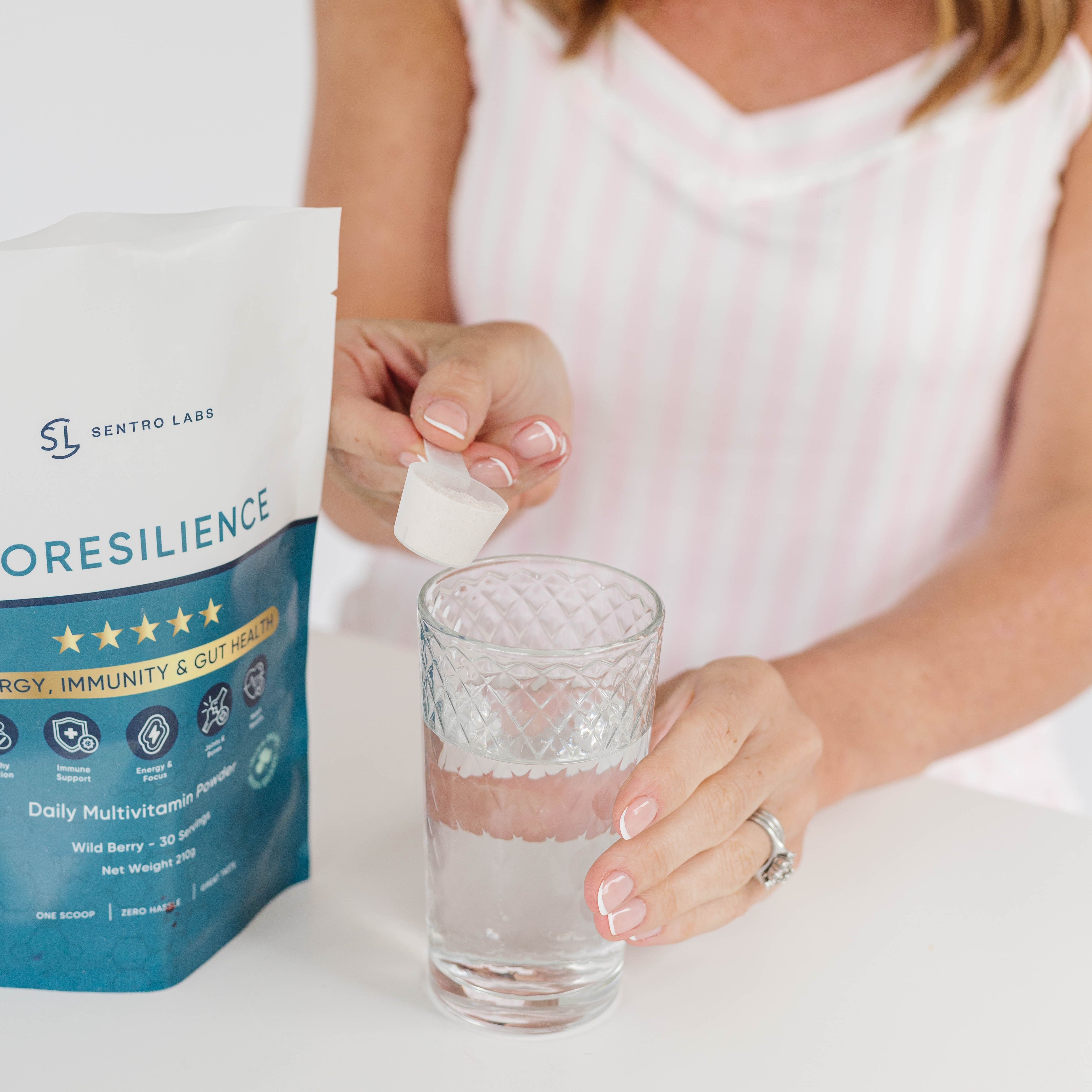 Woman pouring a supplement into a glass of water with a SENTRO LABS BIORESILIENCE package on a white background.
